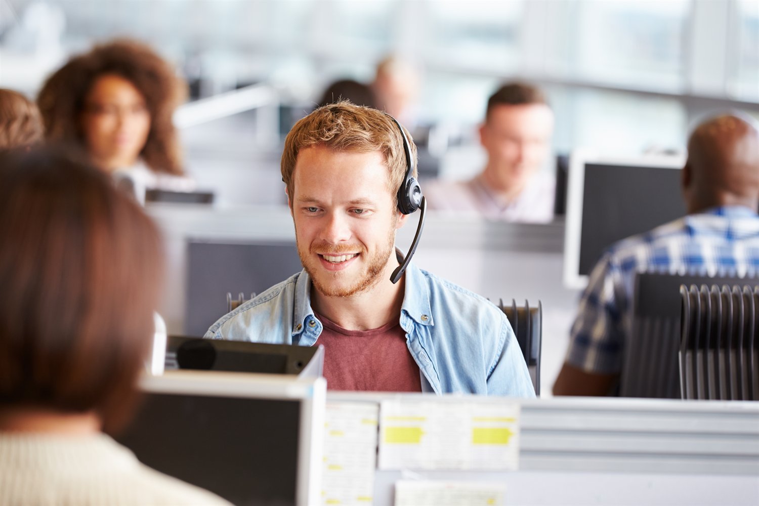 Automatic Call Distribution (ACD) Agent with a headset in a busy open-plan contact centre where automatic call distribution shares calls between the team